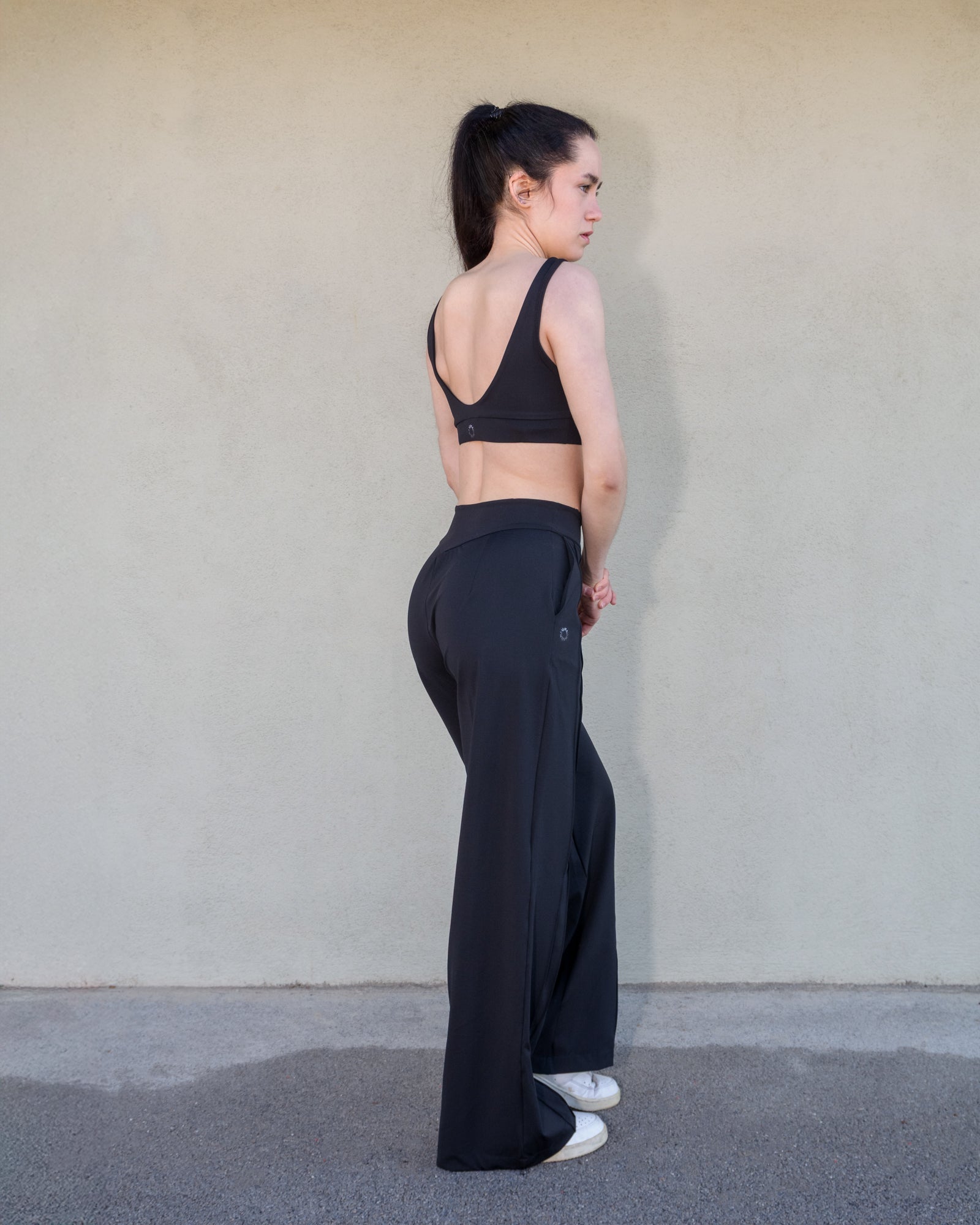 Vista trasera 3/4 del look deportivo Vima Studio. Sujetador deportivo Camelia con escote pronunciado y goma en la cinturilla. Pantalón holgado Azalea