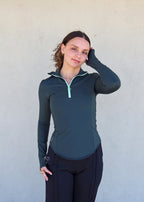 Sudadera ajustada "Magnolia" de Vima Studio en verde. Cuello alto abierto con cremallera visible. Mangas largas con abertura para el pulgar.