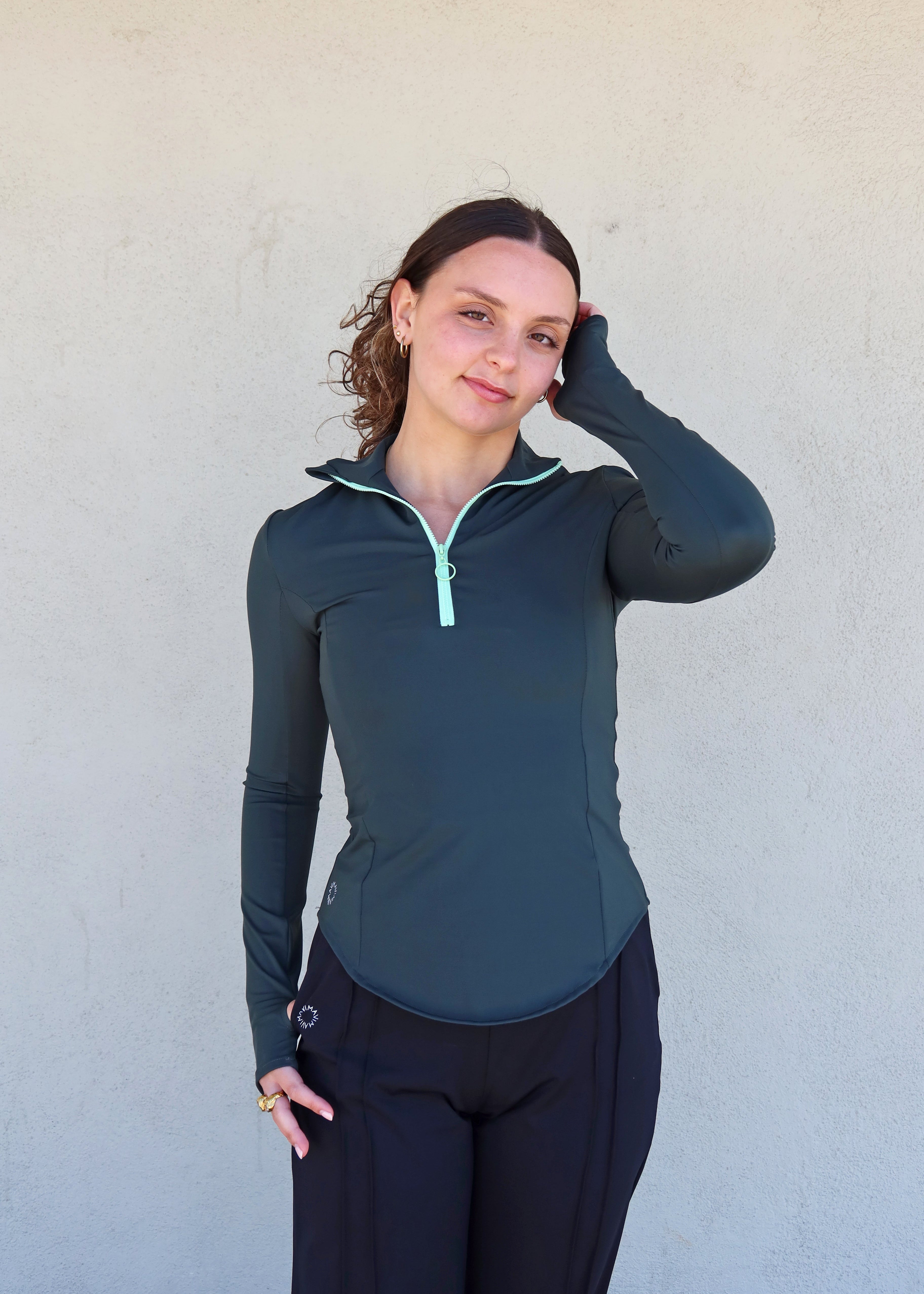 Sudadera ajustada "Magnolia" de Vima Studio en verde. Cuello alto abierto con cremallera visible. Mangas largas con abertura para el pulgar.