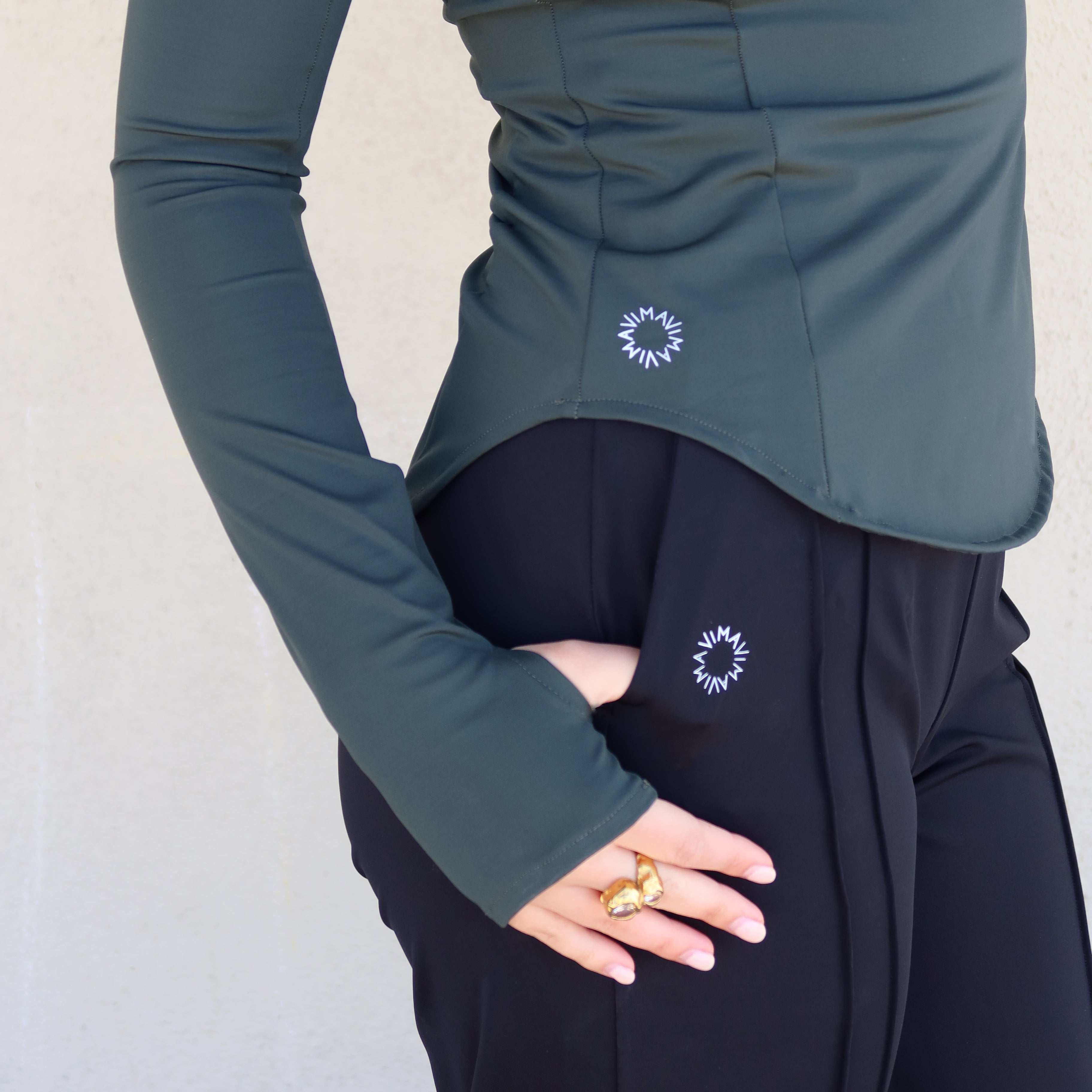 Detalle de perfil de la Sudadera Magnolia en verde – bajo redondeado, logo en costadillo y hueco para el pulgar en manga larga. Vima Studio.