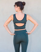 Espalda del top deportivo Amapola en verde con el legging ajustado Dalia de Vima Studio. Escote pronunciado, apertura medialuna y vivos a contraste.