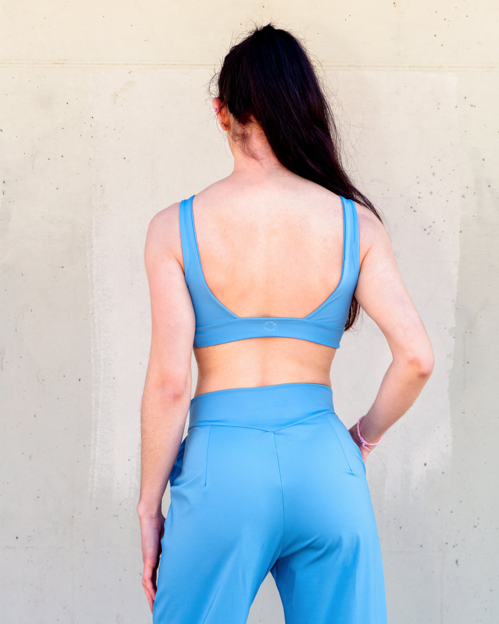Vista trasera del sujetador deportivo Camelia en azul. Espalda abierta, tirantes anchos y buen soporte. Con pantalón con pinzas Azalea. Vima Studio